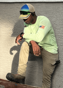 A man in green shirt and hat sitting on the ground.